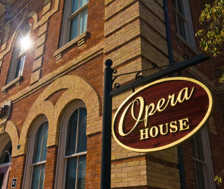 Sign reading "Opera House" set in front of a two toned brick historic building